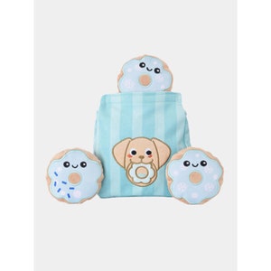 May include: A dog-themed plush toy set featuring a light blue striped bag with a puppy applique and three donut-shaped toys. The donuts have blue frosting and sprinkles, with smiling faces.