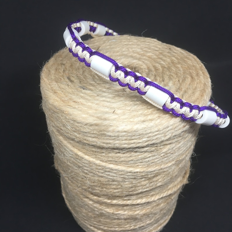 May include: A white and purple braided bracelet with white beads.