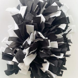 May include: A handmade pet bed or mat made of black and white felt strips. The strips are cut into rectangular shapes and arranged in a layered, shaggy design. The color scheme is monochromatic, with a mix of black and white.