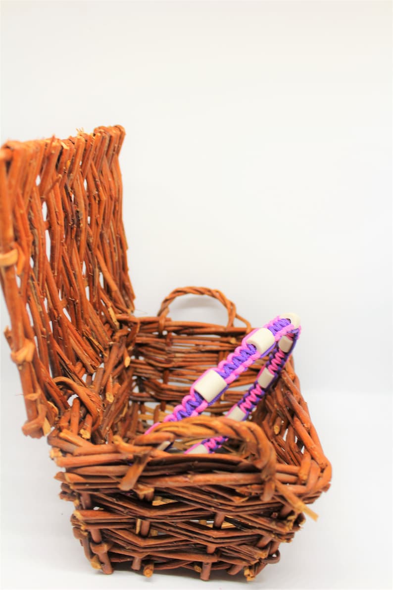 May include: A woven wicker basket with a purple and pink braided bracelet with white beads inside.