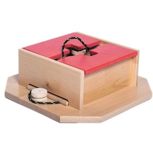 May include: A wooden box with a red lid and a cross-shaped opening. A string is threaded through the opening and tied to a wooden spool.