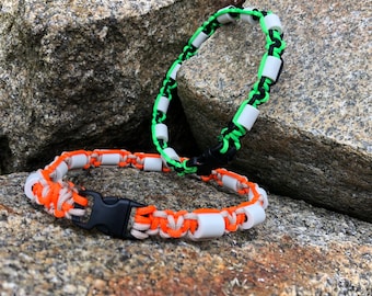 May include: Two paracord bracelets with white beads. One bracelet is black and green, the other is orange and tan.