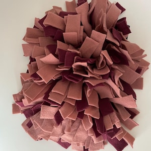 May include: A pink and burgundy felt dog toy with a variety of strips of felt sewn together to create a textured surface.