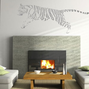 May include: A gray and white tiger silhouette wall decal above a fireplace with a lit fire. The decal is on a white wall. The fireplace is made of stone and has a black metal surround. There are two couches on either side of the fireplace.