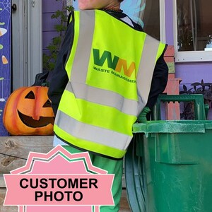 Peut inclure: Un jeune portant un gilet de s&eacute;curit&eacute; jaune et vert avec le logo "WM Waste Management" tient une poubelle de recyclage verte. La personne porte une chemise noire et un pantalon vert.