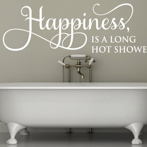 Op de afbeelding: Wit bad met een witte vinyl sticker op de muur erboven met de tekst "Happiness is a long hot shower..."