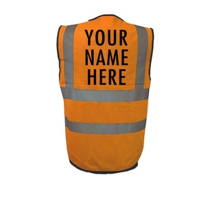 Op de afbeelding: Oranje veiligheidsvest met reflecterende strepen en de tekst "YOUR NAME HERE" gedrukt op de achterkant.
