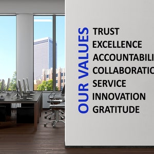 May include: A white wall with the words "OUR VALUES" in blue vertical text and the following words in black horizontal text: TRUST, EXCELLENCE, ACCOUNTABILITY, COLLABORATION, SERVICE, INNOVATION, GRATITUDE.