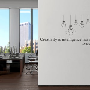 May include: A white wall with a black and white quote that reads "Creativity is intelligence having fun -Albert Einstein". The quote is accompanied by a drawing of five light bulbs hanging from the ceiling.