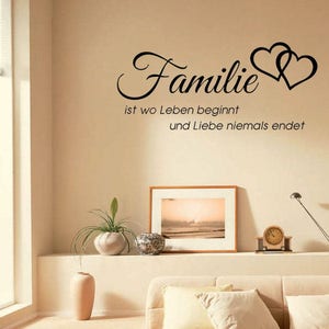Puede incluir: Una calcoman&iacute;a de pared con el texto "Familie ist wo Leben beginnt und Liebe niemals endet" en letras negras. El texto est&aacute; acompa&ntilde;ado por dos corazones entrelazados.