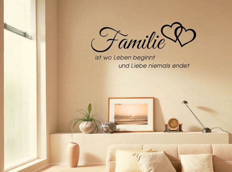 Puede incluir: Una calcoman&iacute;a de pared con el texto "Familie ist wo Leben beginnt und Liebe niemals endet" en letras negras. El texto est&aacute; acompa&ntilde;ado por dos corazones entrelazados.