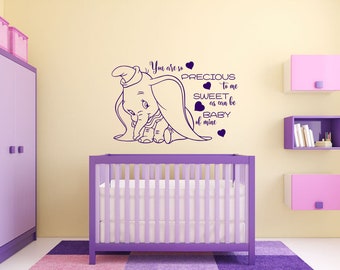 Puede incluir: Un vinilo decorativo morado con Dumbo el elefante y el texto "You are so precious to me, sweet as can be, baby of mine." El vinilo está colocado sobre una cuna morada en un cuarto de bebé.