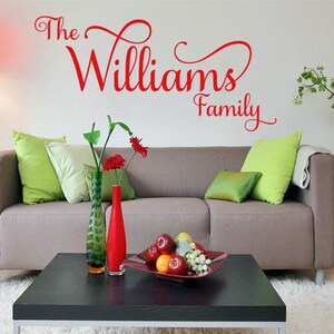 May include: A living room with a grey sofa and a black coffee table. The wall has a red vinyl decal that reads "The Williams Family".