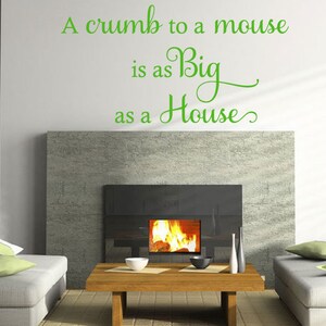Op de afbeelding: Een groene vinyl wand sticker met de tekst "A crumb to a mouse is as Big as a House". De sticker is geplaatst boven een open haard in een woonkamer.