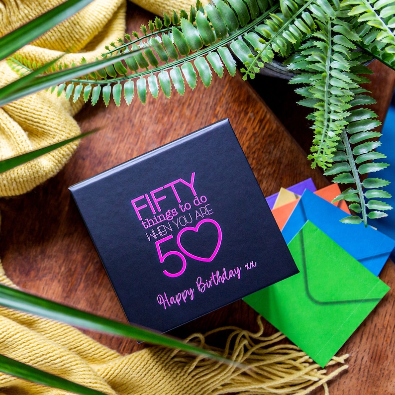 K&ouml;nnte beinhalten: Eine schwarze Geschenkbox mit einem rosa Herzen und dem Text "FIFTY things to do when you are 50 Happy Birthday xx".