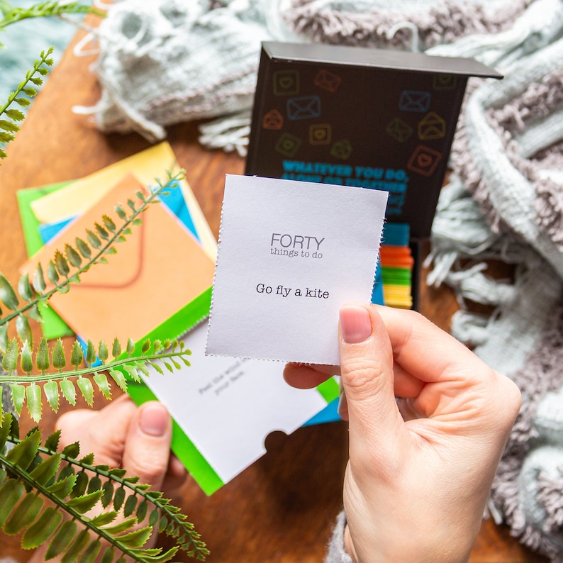 Pu&ograve; includere: Una carta bianca con il testo "FORTY things to do" e "Go fly a kite" su di essa. La carta &egrave; tenuta da una mano. La carta fa parte di un set di gioco con altre carte sullo sfondo.