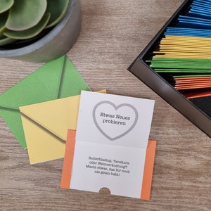 Könnte beinhalten: Eine weiße Karte mit einer Herzform und dem Text "Etwas Neues probieren". Die Karte enthält auch den Text "Rollerblading, Tanzkurs oder Weinverkostung? Macht etwas, das Ihr noch nie getan habt!"