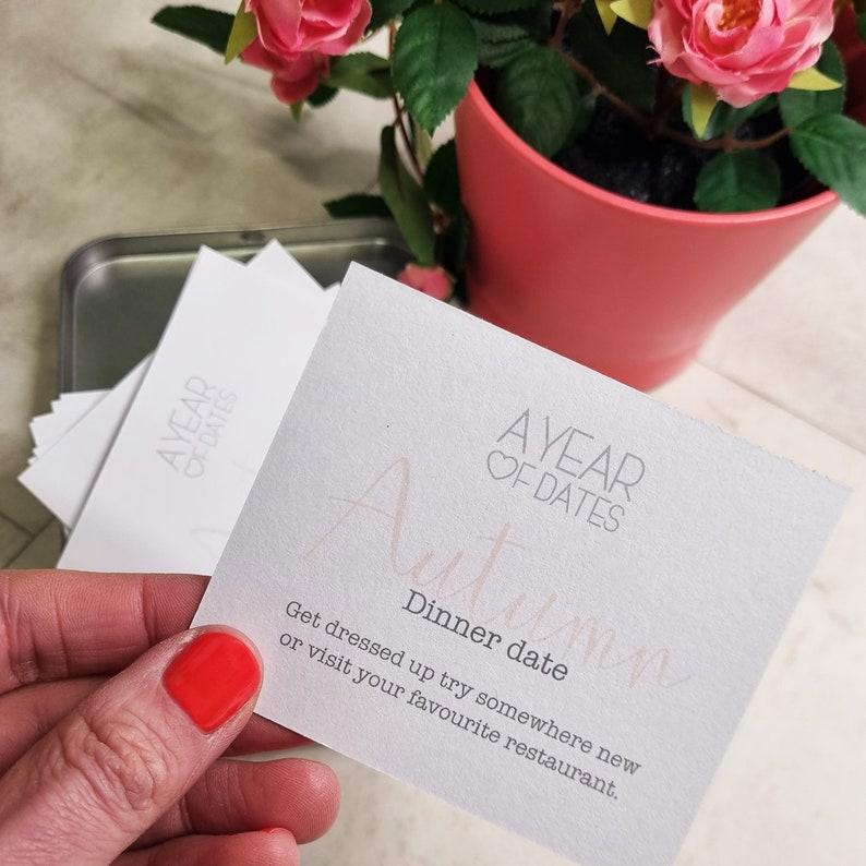 May include: A white card with the text "AYEAR OF DATES" and the handwritten word "Autumn" in pink. The card also includes the text "Dinner date" and "Get dressed up try somewhere new or visit your favourite restaurant."