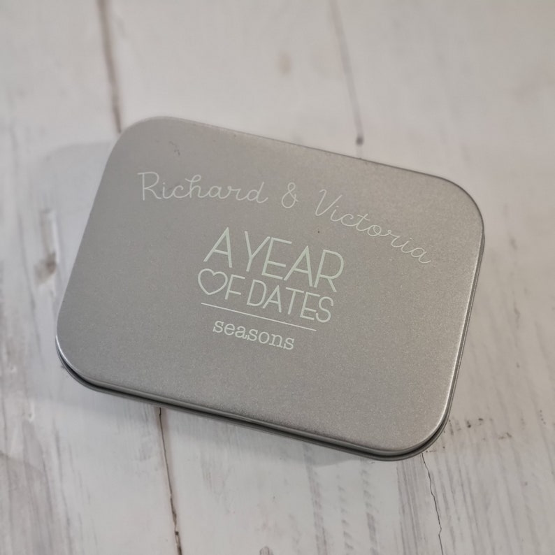 May include: A silver metal tin with the text "Richard & Victoria A YEAR OF DATES seasons" printed on the top.