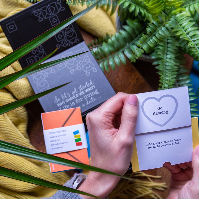 May include: A set of cards with a gray and black cover. The cover has a design of envelopes and hearts. The cards are open to reveal a white card with a gray heart and the text "Go dancing". The text below the heart reads "Take a salsa class or dance the night away in a club."