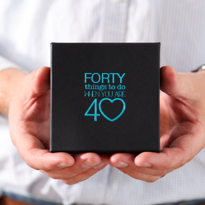 Pu&ograve; includere: Una scatola nera con il testo "FORTY things to do when you are 40" in blu con un cuore blu.