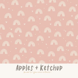 Op de afbeelding: Een herhalend patroon van crèmekleurige regenbogen en kleine hartjes op een lichtroze achtergrond. De tekst "Apples + Ketchup" staat onderaan, met daaronder "kid's favorites".