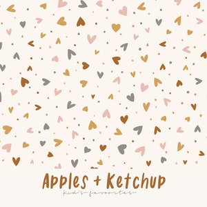 Op de afbeelding: Een crèmekleurige achtergrond met een patroon van kleine hartjes in tinten bruin, goud, grijs en roze. Kleine stippen in vergelijkbare kleuren zijn verspreid. De tekst "Apples + Ketchup" is in bruin geschreven, met "kid's favorites" eronder.