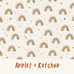 Op de afbeelding: Een herhalend patroon van bruine, grijze en roze regenbogen, met kleine hartjes en stippen op een crèmekleurige achtergrond. De tekst "Apples + Ketchup" staat onderaan.