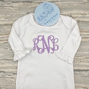 May include: White long-sleeved baby gown with a purple embroidered monogram "RNC" and a blue and white tag that reads "Gingham & Pearls est. 2016".