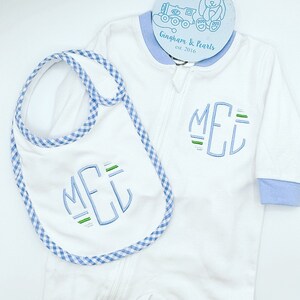 May include: White baby onesie with a blue and green monogram "MEL" embroidered on the front. A matching blue and white gingham bib with the same monogram is included. The onesie has a blue trim around the neck and wrists. The tag on the onesie reads "Gingham & Pearls est. 2016".