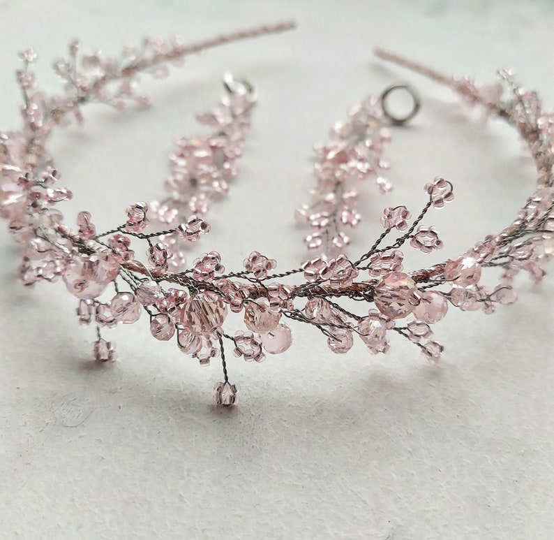 May include: A delicate pink beaded headband with a floral design. The headband is made of wire and features small pink beads and crystals.