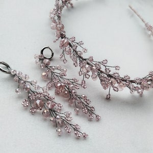 May include: A delicate bridal hairpiece and matching earrings with a floral design made of pink crystal beads and silver wire.