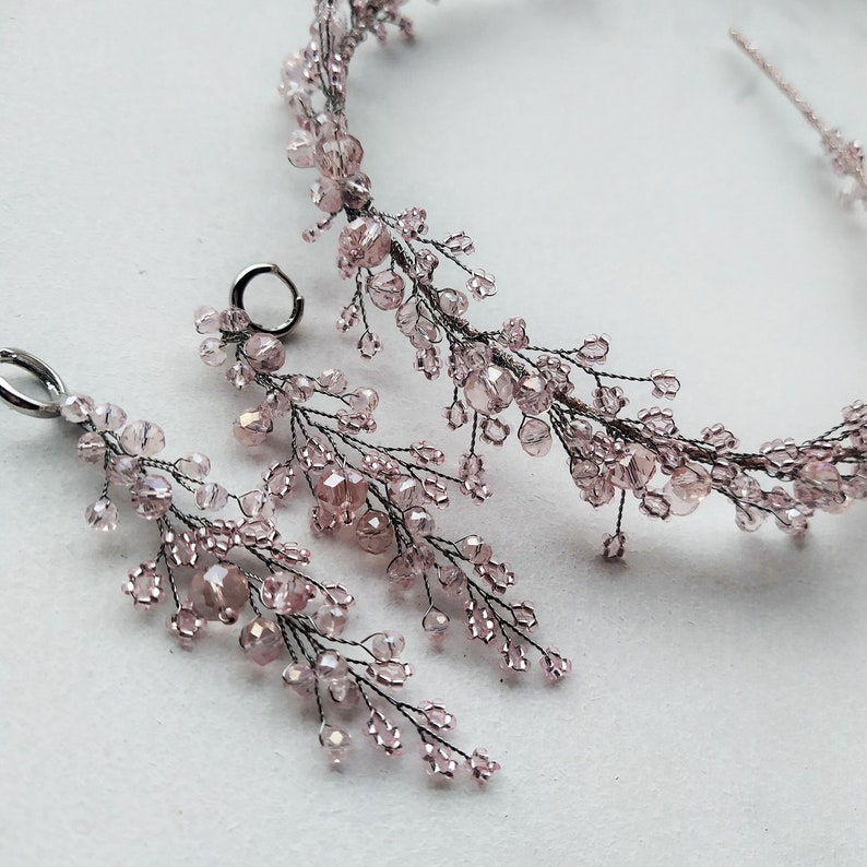 May include: A delicate bridal hairpiece and matching earrings with a floral design made of pink crystal beads and silver wire.