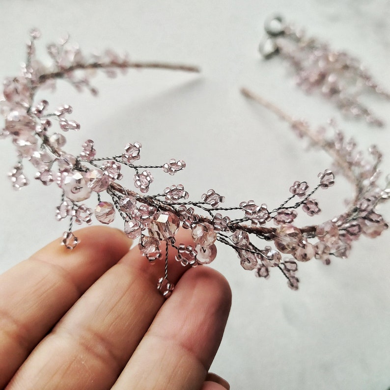 May include: A delicate pink and silver beaded headband with a floral design. The headband is made of wire and features small pink beads and larger clear beads.