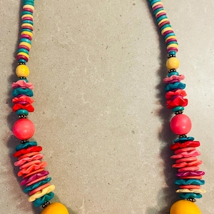 May include: A colorful necklace featuring a variety of beads in shades of turquoise, yellow, pink, red, and purple. The necklace has a mix of round and disc-shaped beads, creating a vibrant and eye-catching accessory.