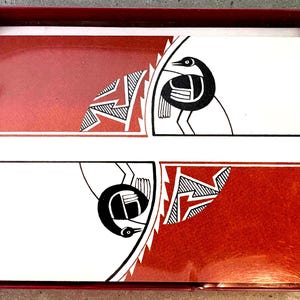 May include: A set of greeting cards in a red box. The cards feature a symmetrical design with a red and white background. The design includes a black bird and geometric shapes.