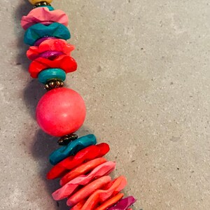 May include: A colorful necklace featuring a variety of beads in shades of pink, yellow, teal, and red. The necklace has a mix of round and disc-shaped beads, creating a vibrant and eye-catching accessory.