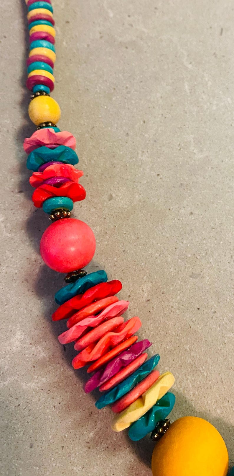 May include: A colorful necklace featuring a variety of beads in shades of pink, yellow, teal, and red. The necklace has a mix of round and disc-shaped beads, creating a vibrant and eye-catching accessory.