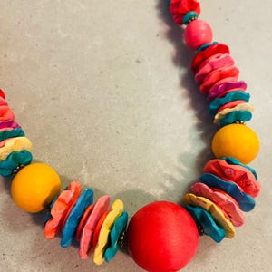May include: A colorful necklace featuring a variety of beads. The necklace includes large, round, yellow and red beads, along with smaller, flower-shaped beads in shades of pink, blue, and yellow. The necklace is strung on a cord.