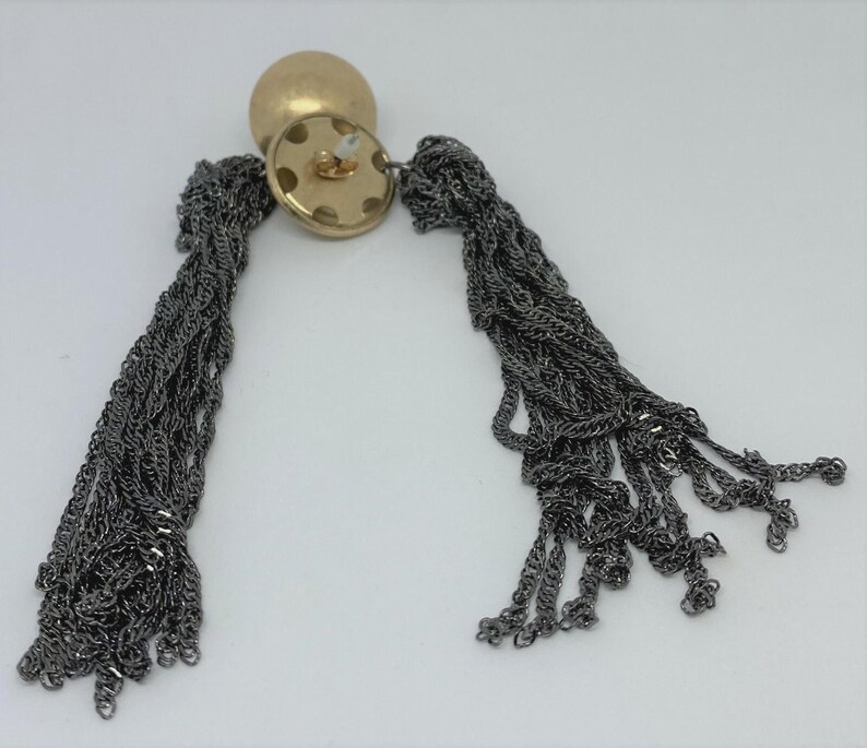 K&ouml;nnte beinhalten: Ein Paar Ohrh&auml;nger mit einem goldfarbenen, runden Stecker und dunkelgrauen Kettenquasten. Die Ohrringe werden vor einem wei&szlig;en Hintergrund pr&auml;sentiert, um ihr Design und ihre Textur hervorzuheben.
