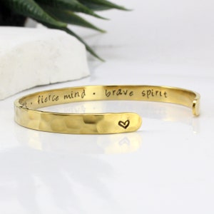 May include: Gold hammered cuff bracelet with the inscription "fierce mind - brave spirit" and a small heart engraved on the side.