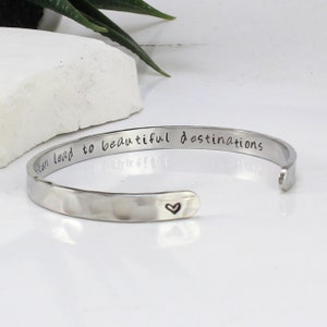 Può includere: Braccialetto rigido in argento con finitura martellata e l'iscrizione "Often lead to beautiful destinations" con un piccolo cuore alla fine.