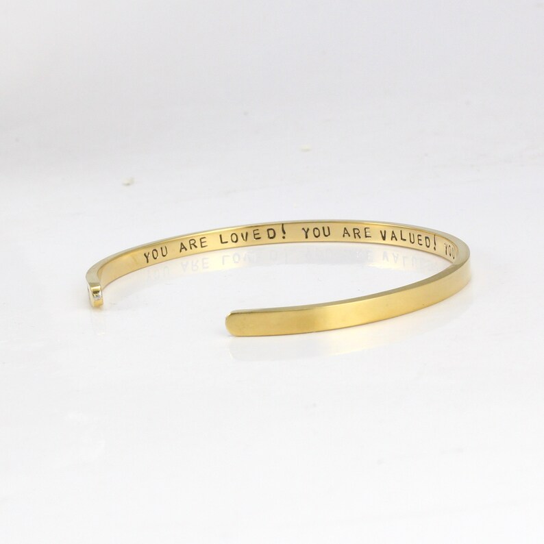 K&ouml;nnte beinhalten: Goldenes Armreif-Armband mit der Inschrift "You are loved! You are valued!"