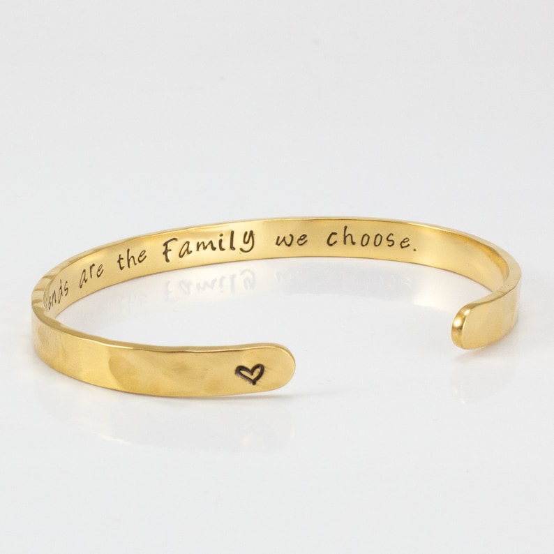 May include: Gold-toned cuff bracelet with the inscription "Friends are the family we choose." and a small heart engraved on the side.