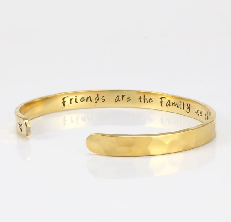 May include: Gold-toned hammered metal cuff bracelet with the inscription "Friends are the family we choose" on the outside and a small heart on the inside.