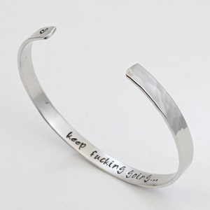 May include: A silver hammered bangle bracelet with the inscription "keep fucking going..."