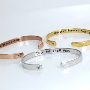 Può includere: Tre braccialetti in metallo martellato con diversi messaggi incisi: "You're my person", "This too shall pass" e "Together forever never apart".