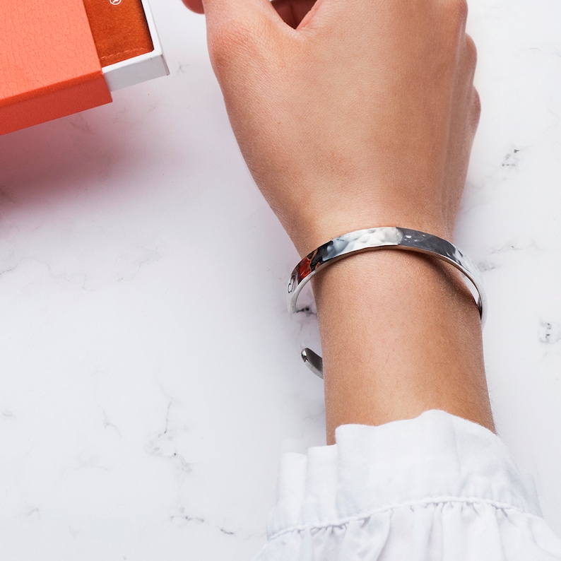 May include: A silver hammered bangle bracelet on a person's wrist.