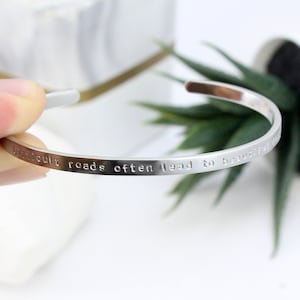 May include: Silver bangle bracelet with the inscription "Difficult roads often lead to beautiful destinations".