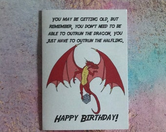 Puede incluir: Tarjeta de cumpleaños blanca con una ilustración de dragón rojo y el texto "YOU MAY BE GETTING OLD, BUT REMEMBER, YOU DON'T NEED TO BE ABLE TO OUTRUN THE DRAGON, YOU JUST HAVE TO OUTRUN THE HALFLING, HAPPY BIRTHDAY!"